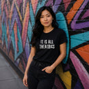 Woman wearing black "It Is All Theatrics" graphic t-shirt outdoors